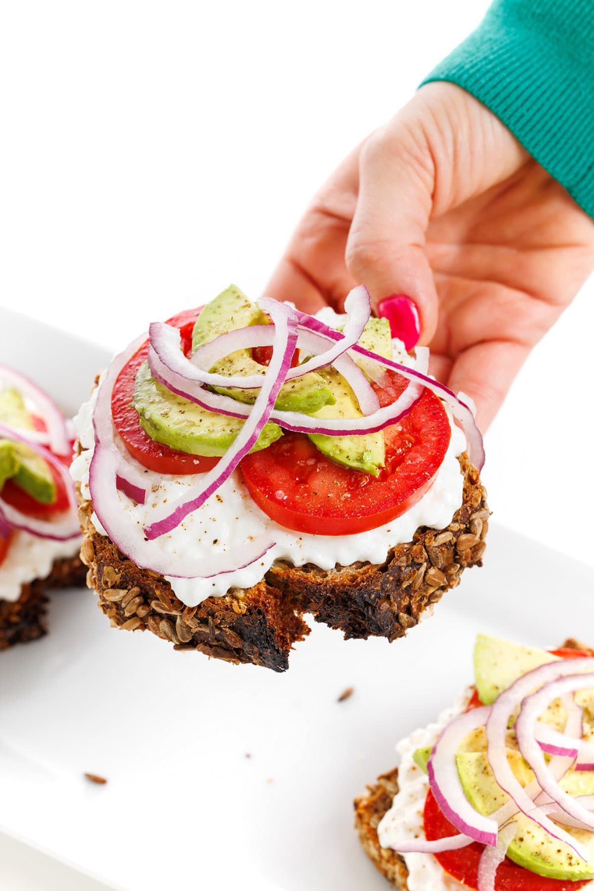 Holding avocado toast with cottage cheese and tomatoes.