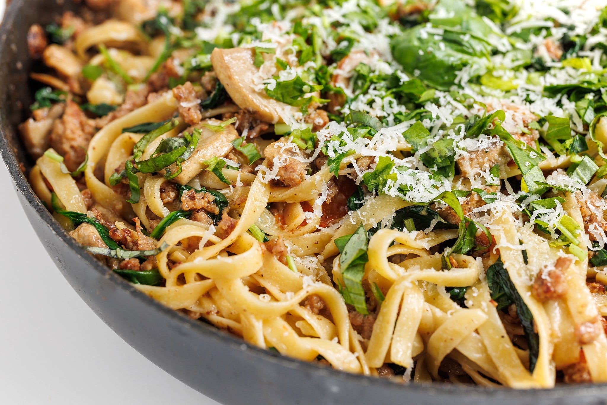 Easy protein one pan dinner: one-pan Italian sausage pasta topped with fresh basil and parmesan cheese.