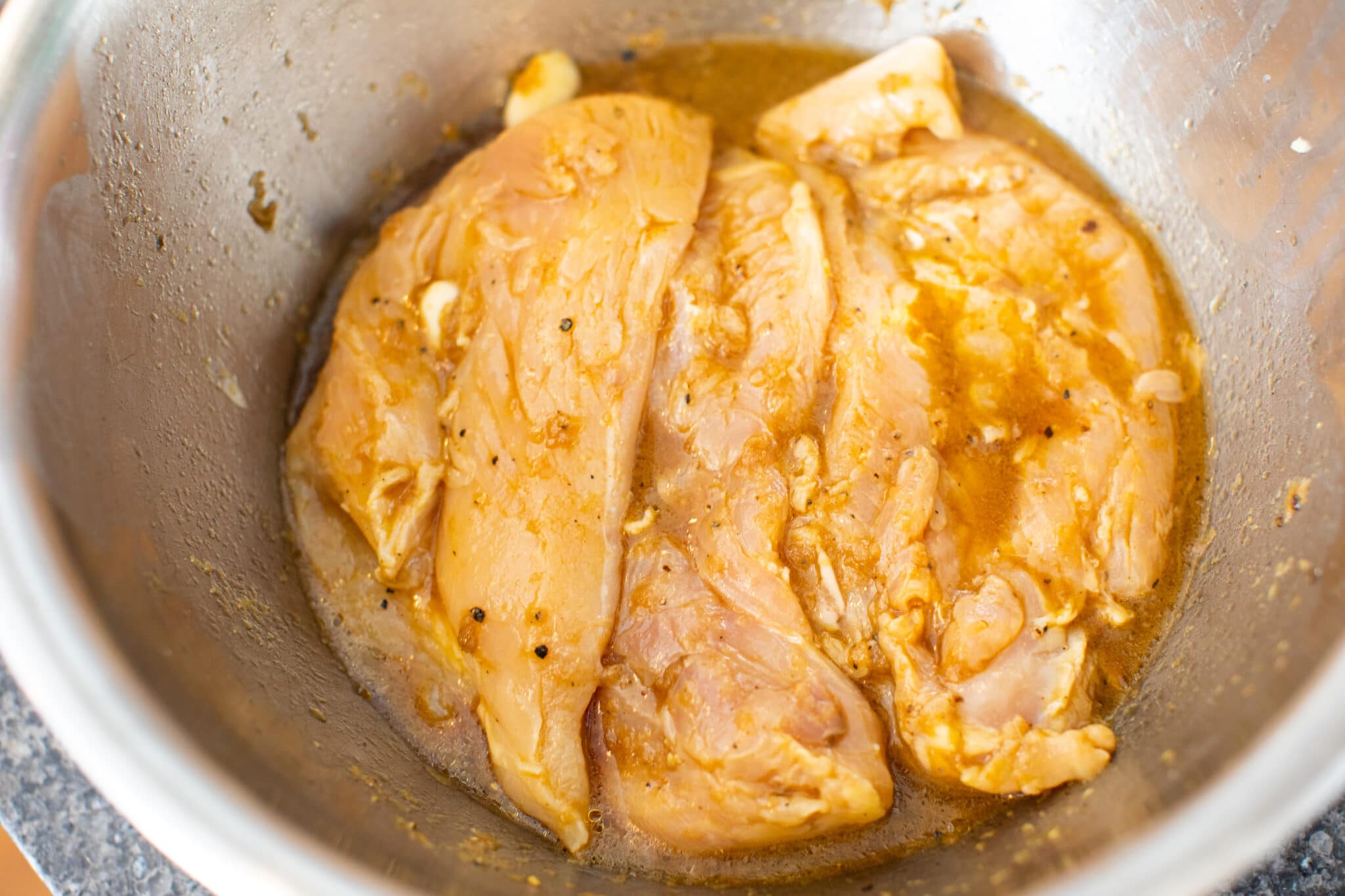 Chicken breasts marinating in bowl.