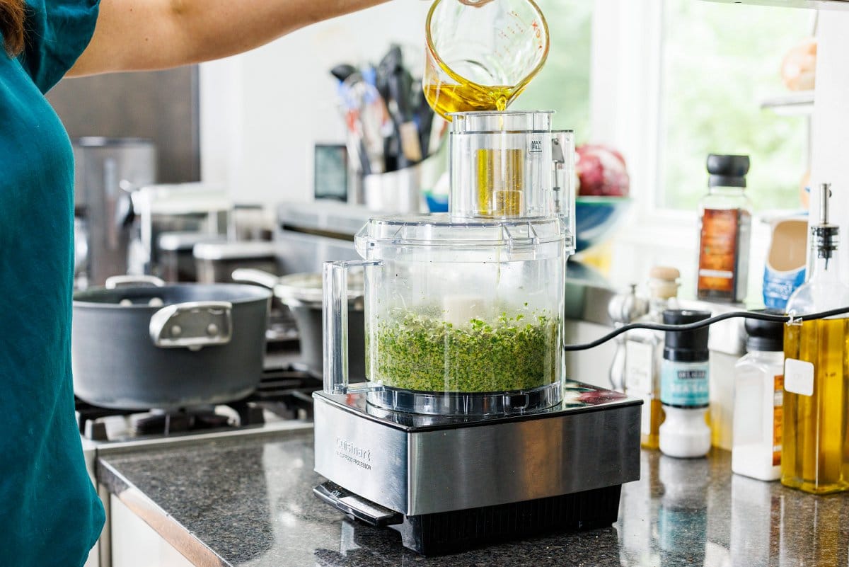 adding olive oil to pesto