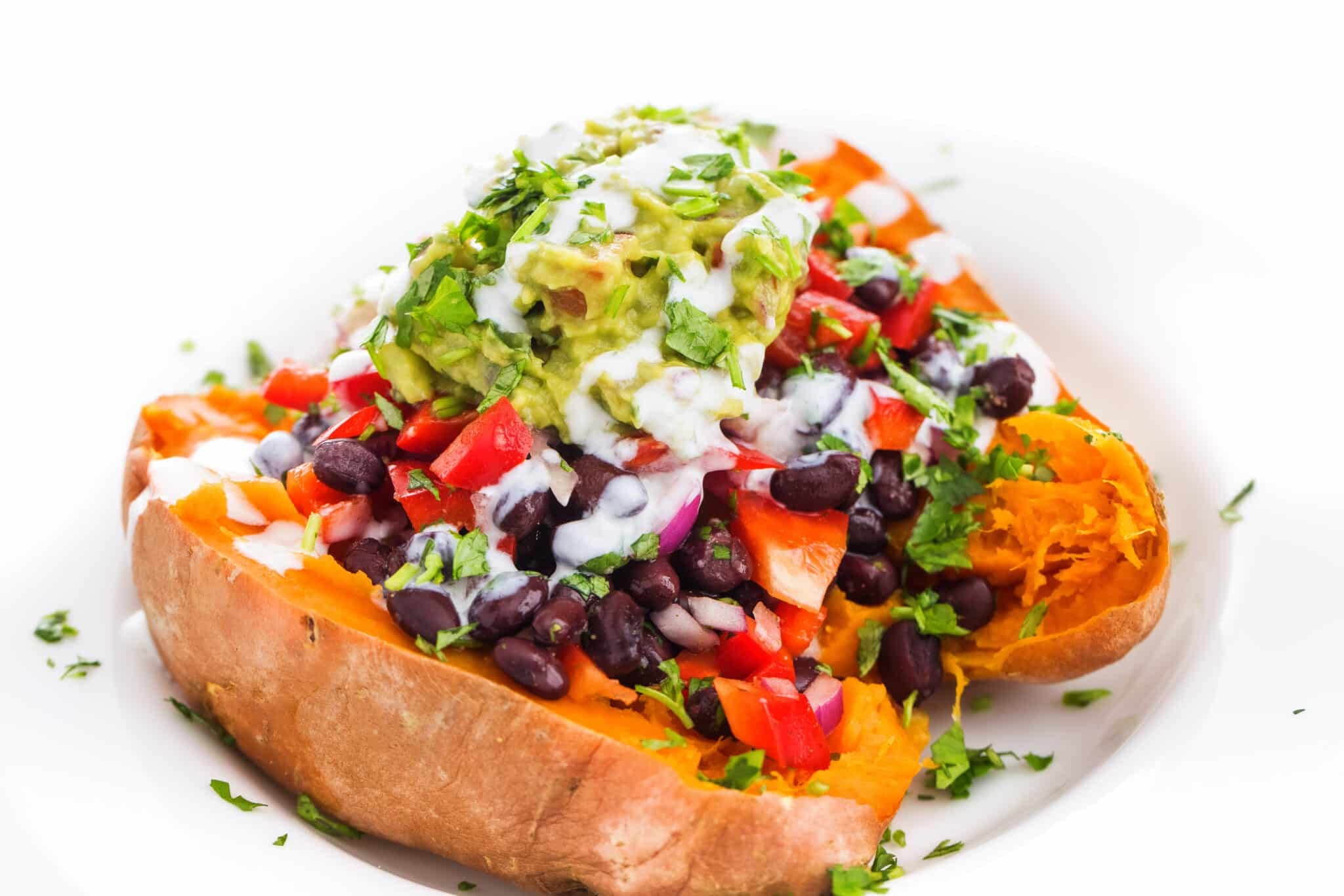A baked sweet potato topped with black beans, guacamole, and fresh herbs.