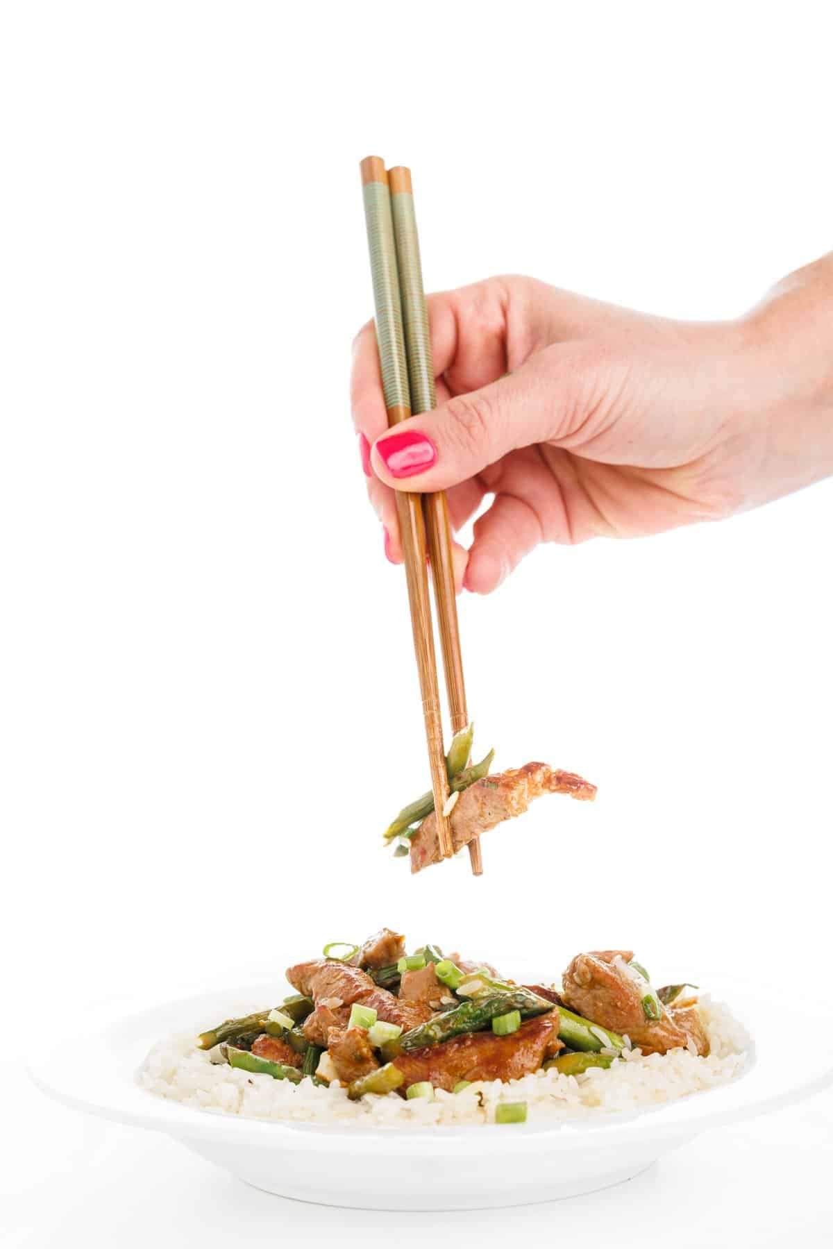Chopsticks picking up pork and asparagus skillet.