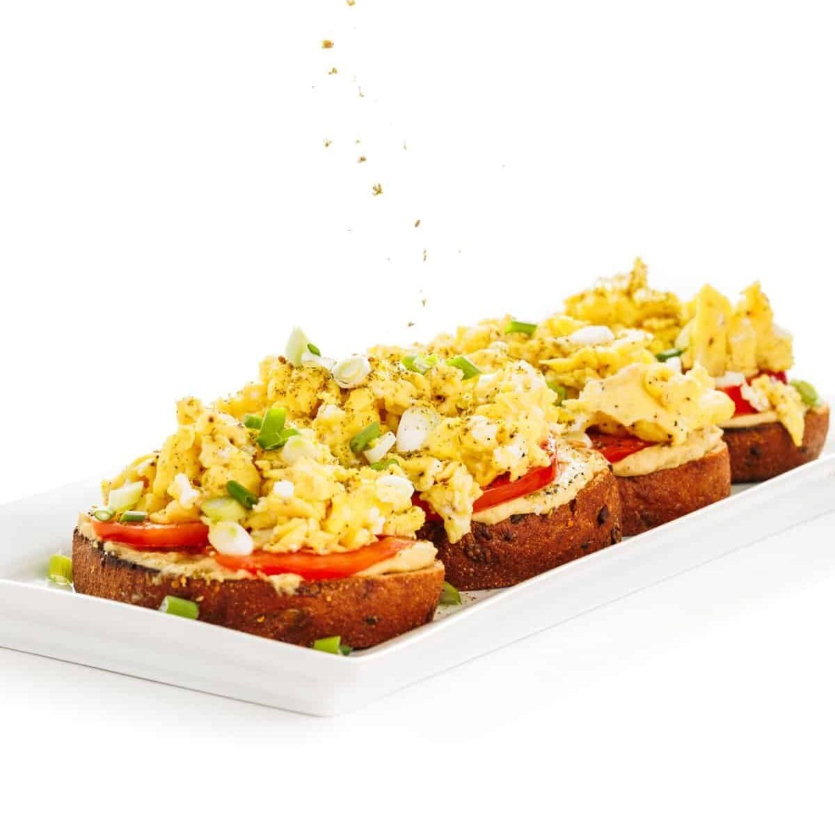 Garnishing hummus toast with scrambled eggs with za'atar.
