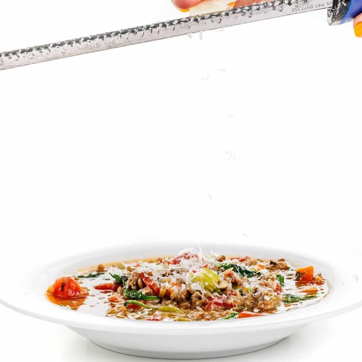 Garnishing lentil soup with sausage and spinach with parmesan cheese.