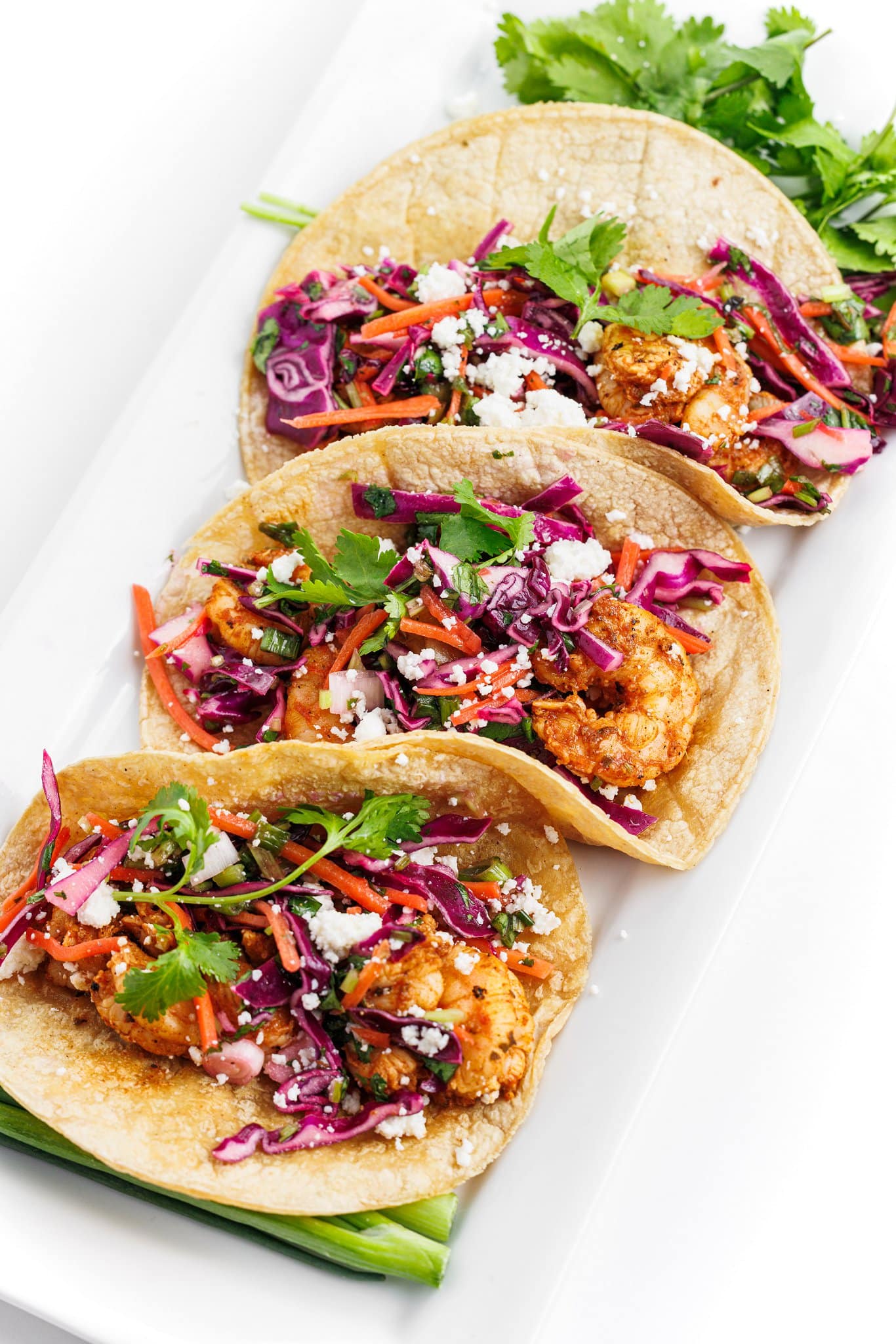 3 grilled shrimp tacos with cabbage slaw arranged on a plate with cilantro as garnish.