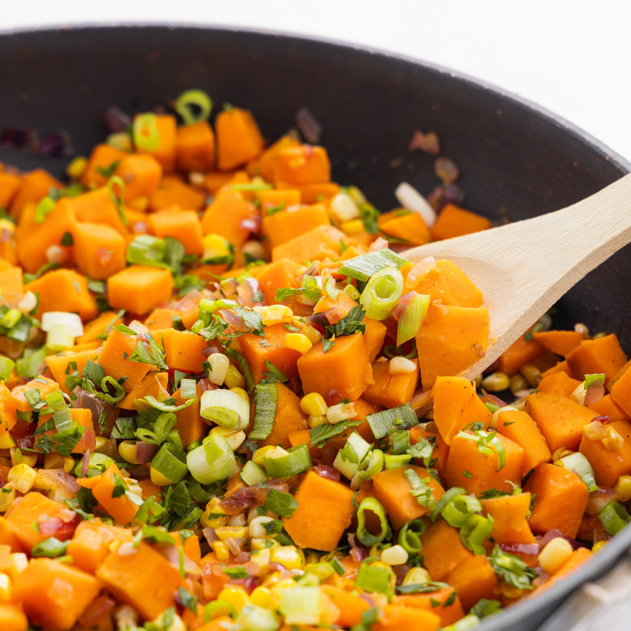 Scooping sweet potato and corn succotash out of cast iron skillet.