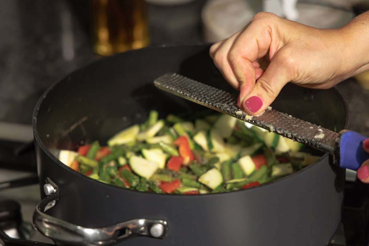 Grating garlic into skillet full of chopped veggies.