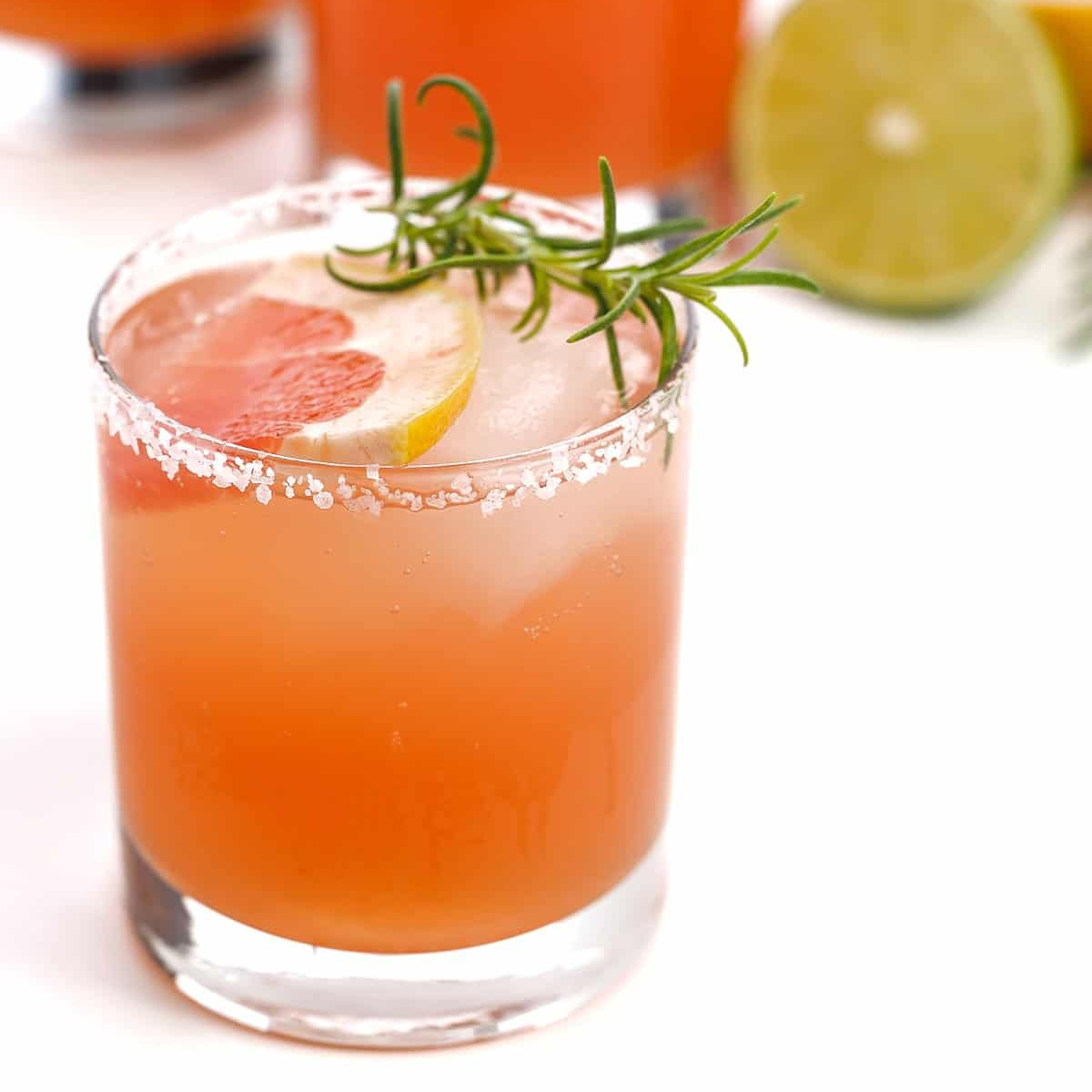 A tumbler of rosemary and gin grapefruit cocktail with a slice of grapefruit and rosemary sprig as garnish.