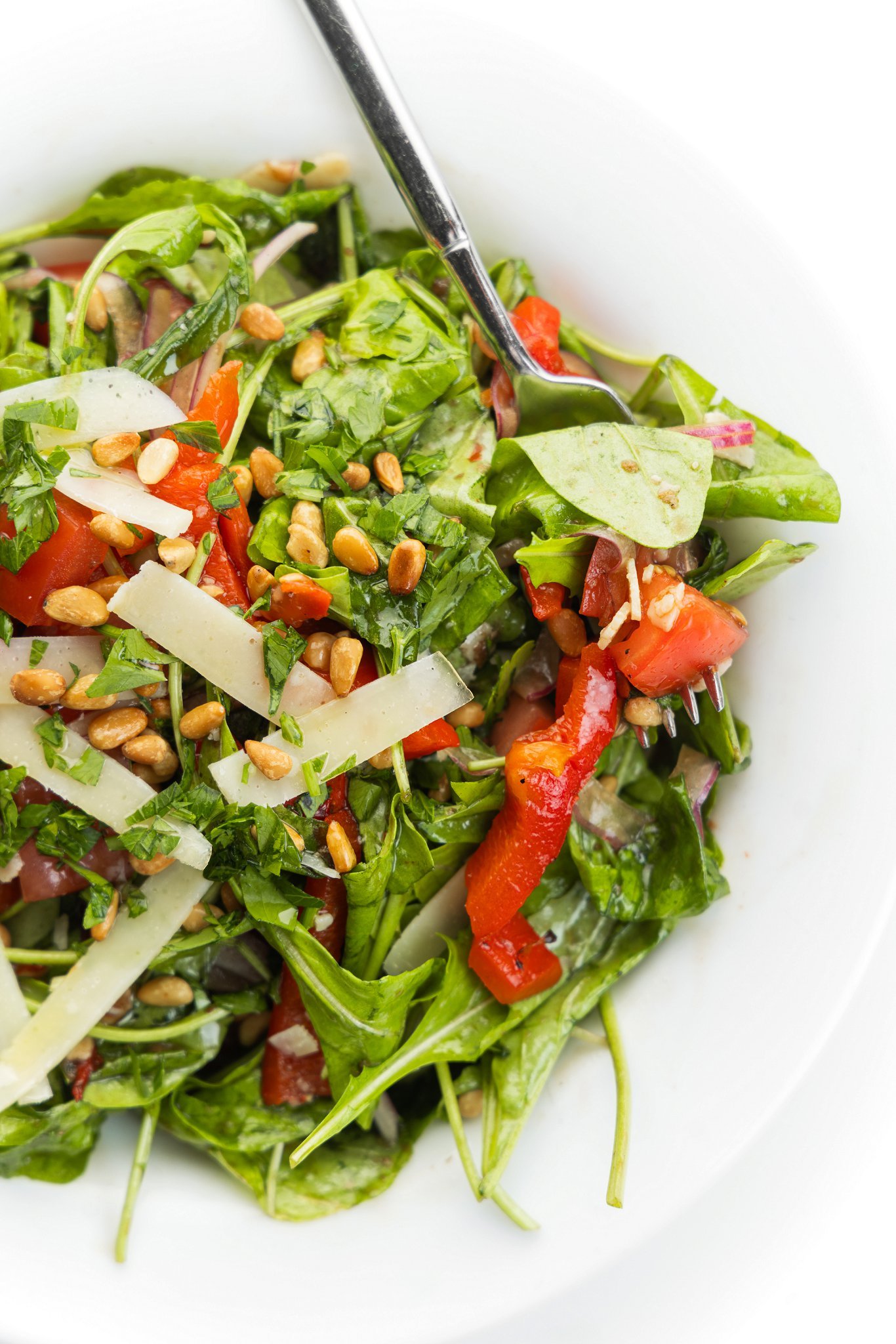 Italian mixed salad with shaved parmesan and toasted pine nuts on a white plate with a fork.