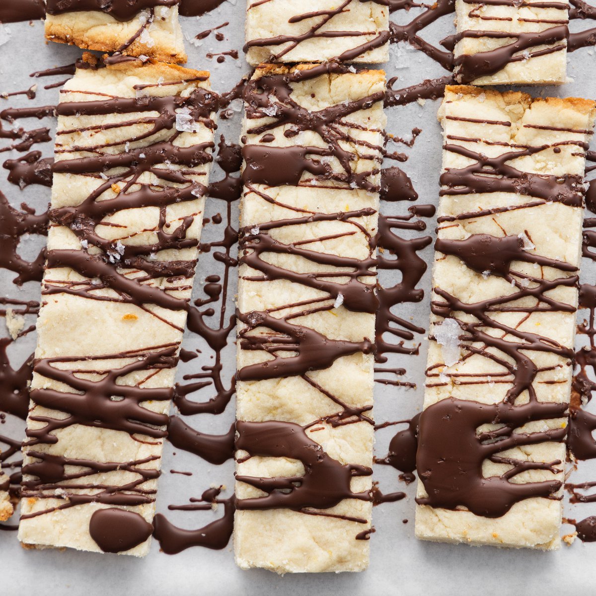 Close up of three lemon shortbread cookies drizzled with chocolate and sprinkled with sea salt.