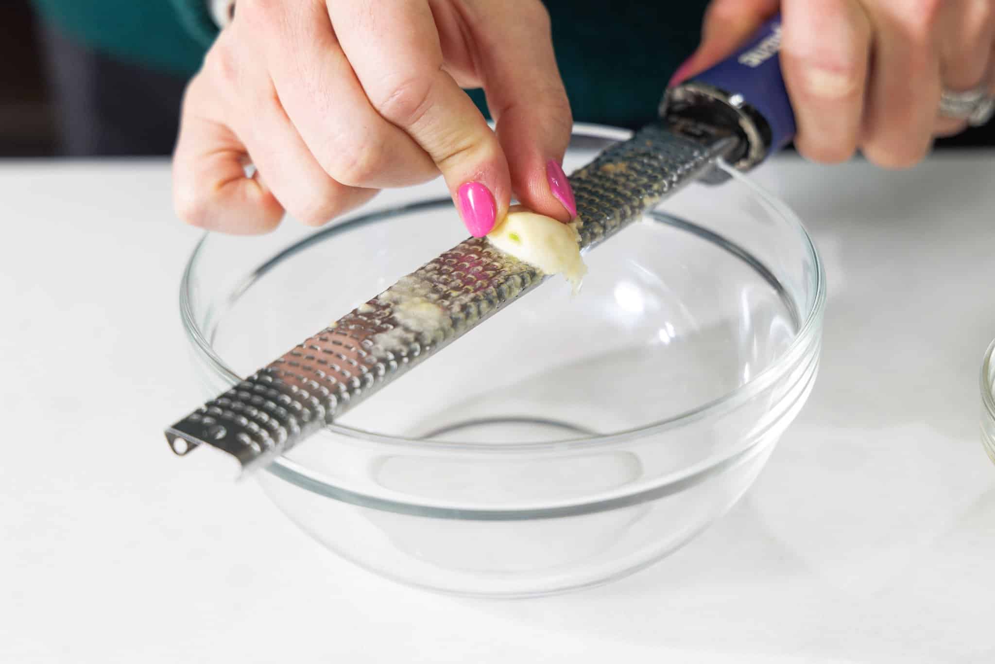 Grating garlic with a microplane into a glass bowl.
