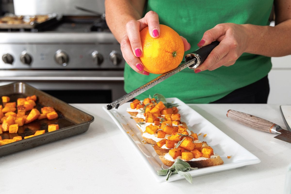 Freshly grating orange zest over the top of crostini.