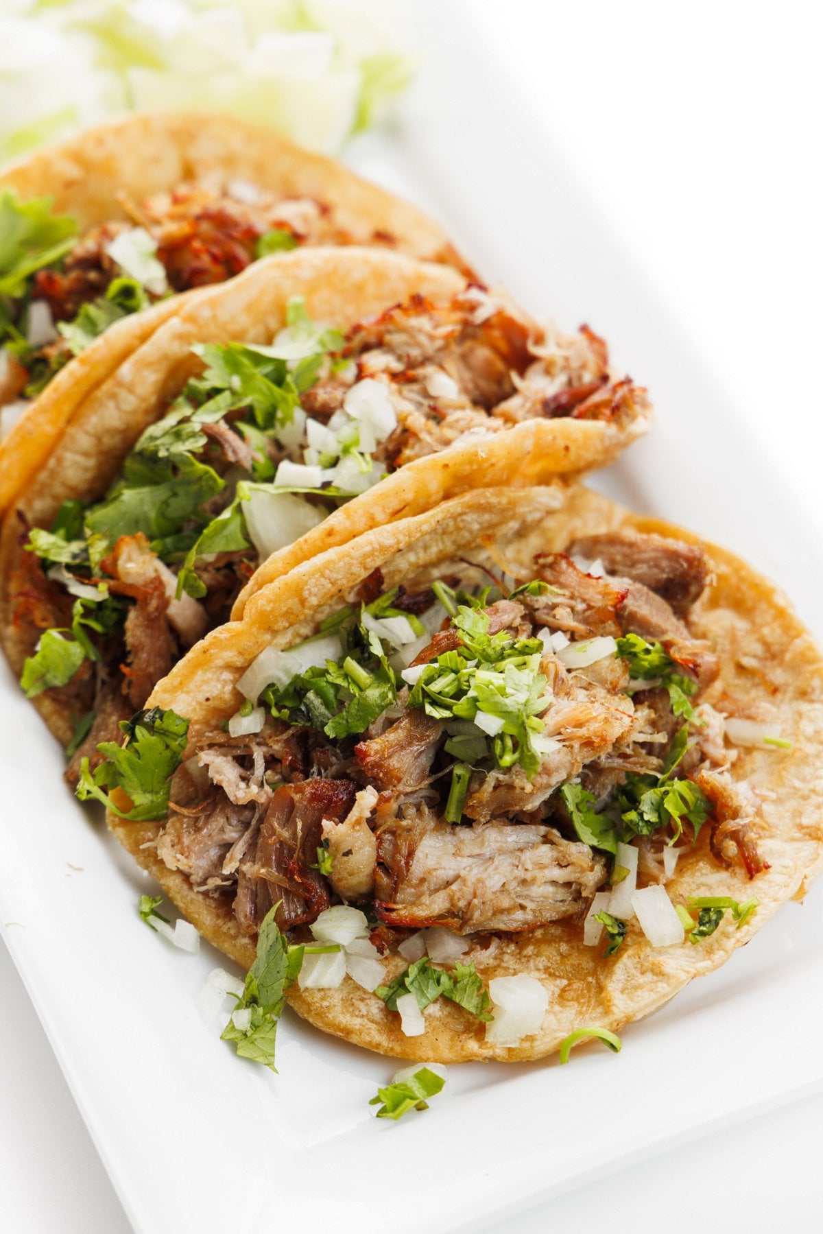 Slow cooker pork carnitas made into tacos on a platter topped with cilantro and diced onion.