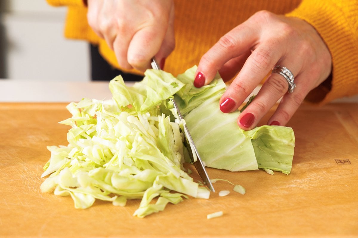 Shredding cabbage on a cutting board with a sharp chefs knife.