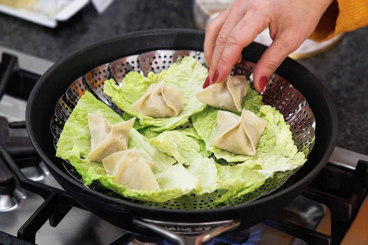 Placing dumplings into a steamer basket lined with cabbage leaves.