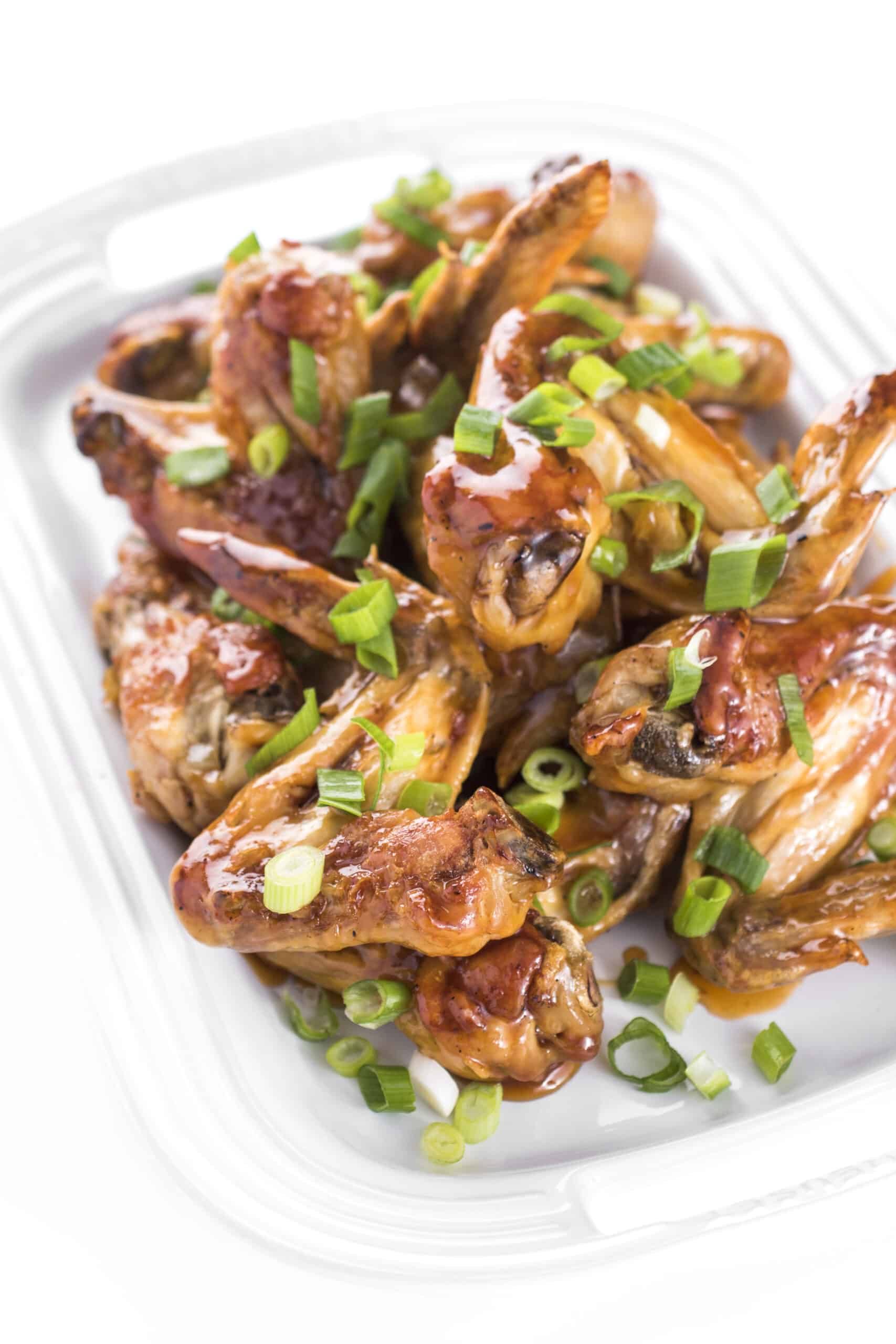 Platter full of crispy oven baked chicken wings sauced and garnished with scallions.