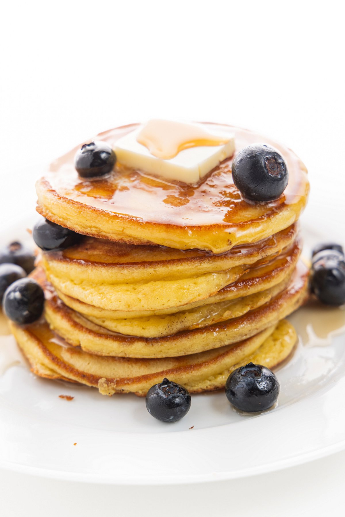 Stack of protein packed pancakes on a plate, topped with a square of butter, syrup, and blueberries.
