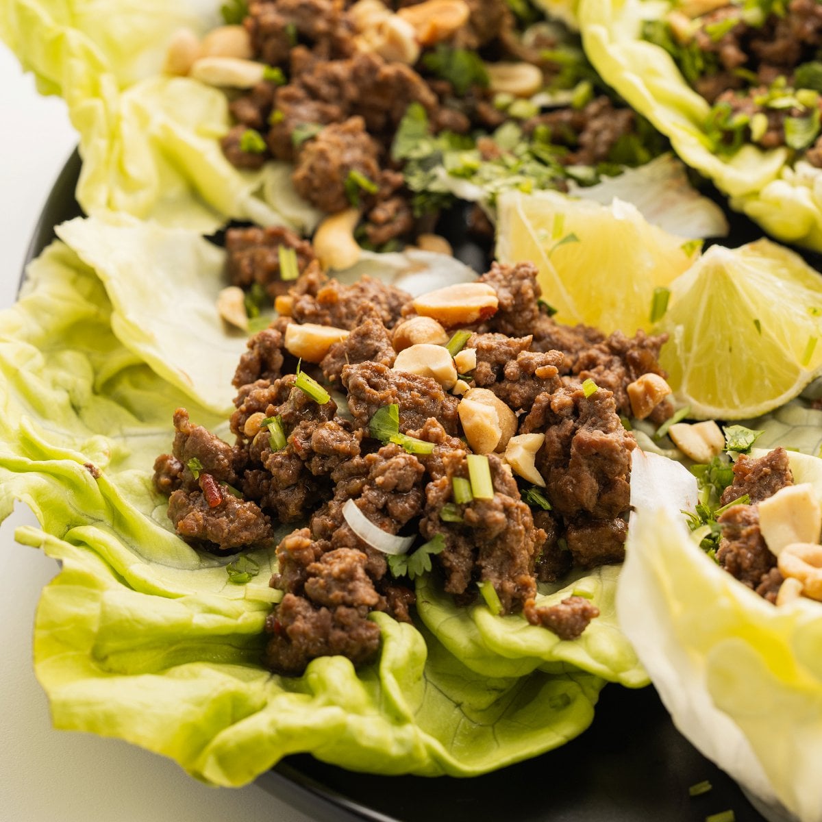 Szechuan Beef Lettuce Wraps on a plate topped with peanuts and fresh scallions.