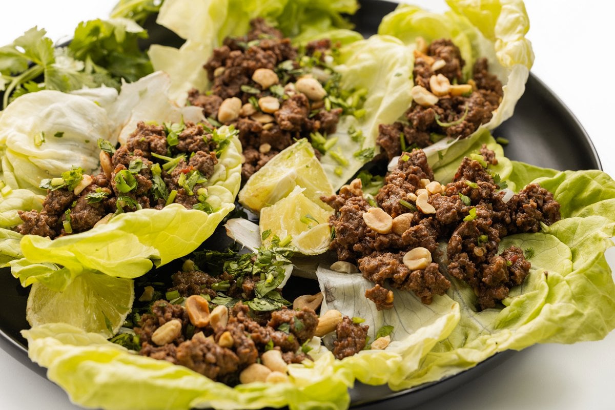 Five Szechuan beef lettuce wraps on a plate with lime wedges.
