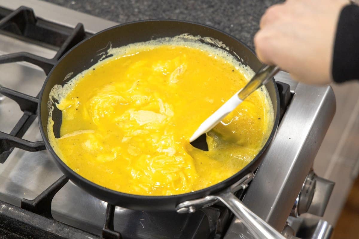 Scrambled eggs cooking in a skillet and being stirred with a spatula.