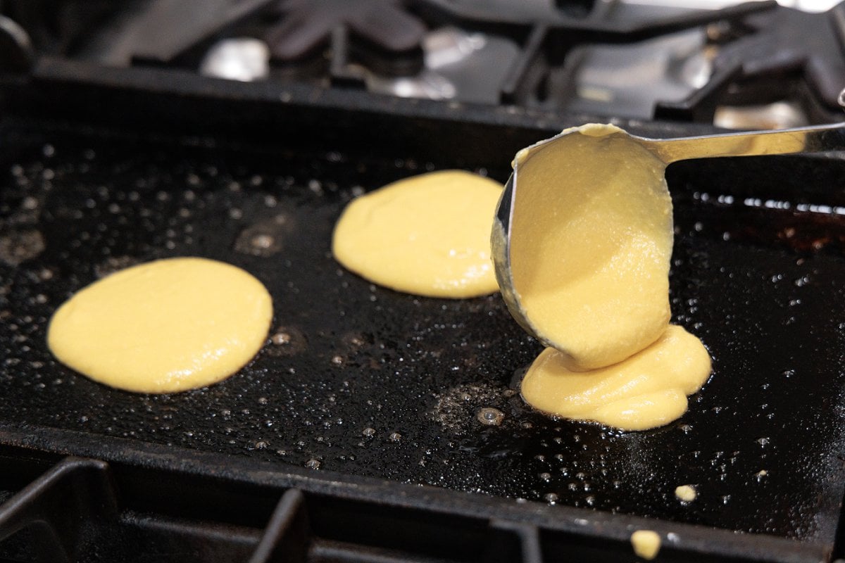 Using a ladle to portion pancake batter onto a hot griddle.