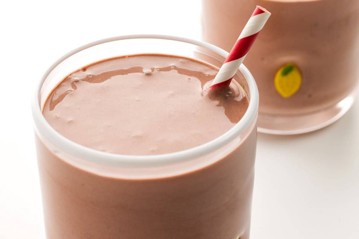 Straw sticking out of a chocolate cherry protein smoothie in a glass tumbler.