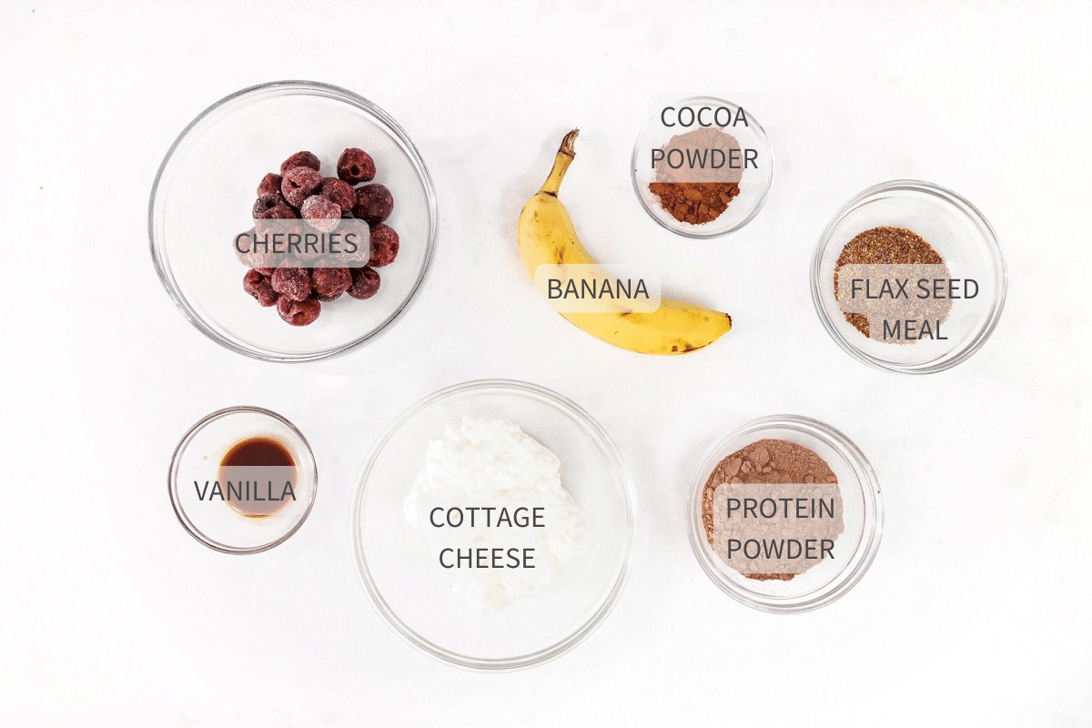 Labeled ingredients for chocolate cherry protein smoothie on a white counter.