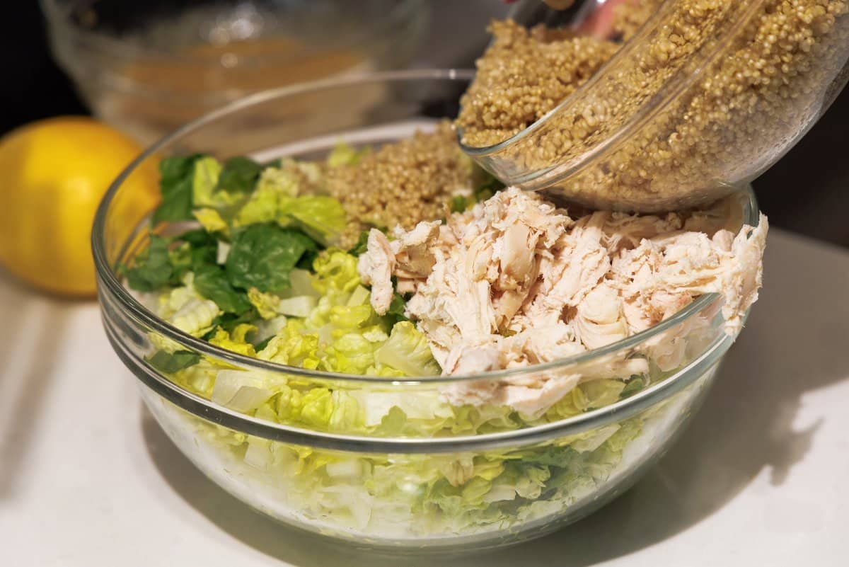 Adding cooked quinoa on top of salad next to chicken.