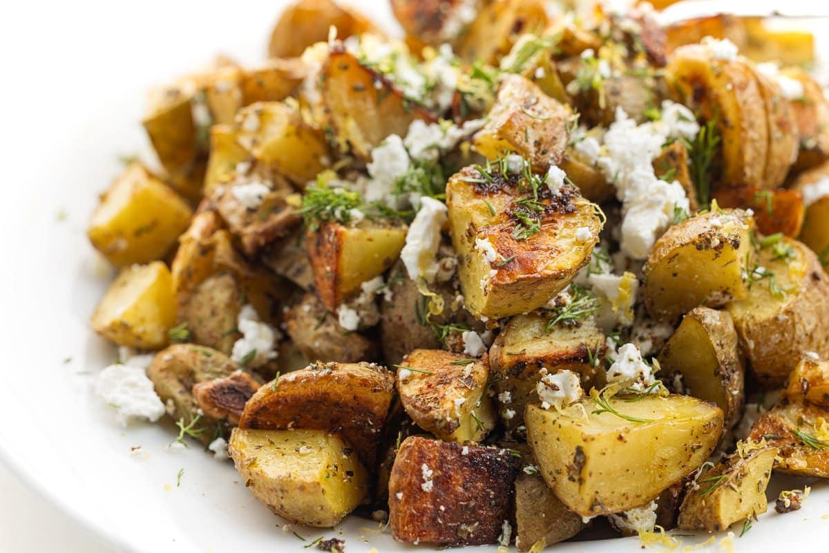 Greek roasted potatoes on a plate garnished with feta and herbs.