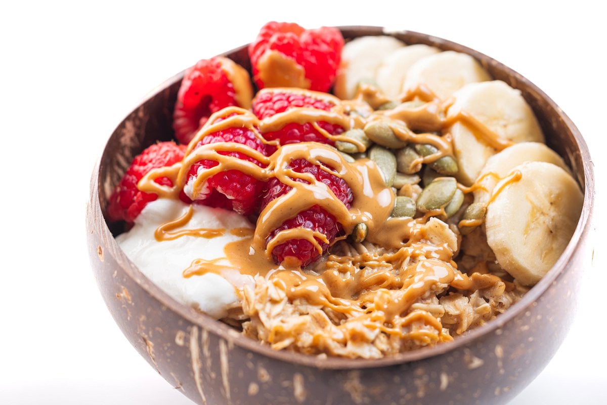 A bowl of 90 second microwave oatmeal topped with raspberries, bananas, and drizzled peanut butter.