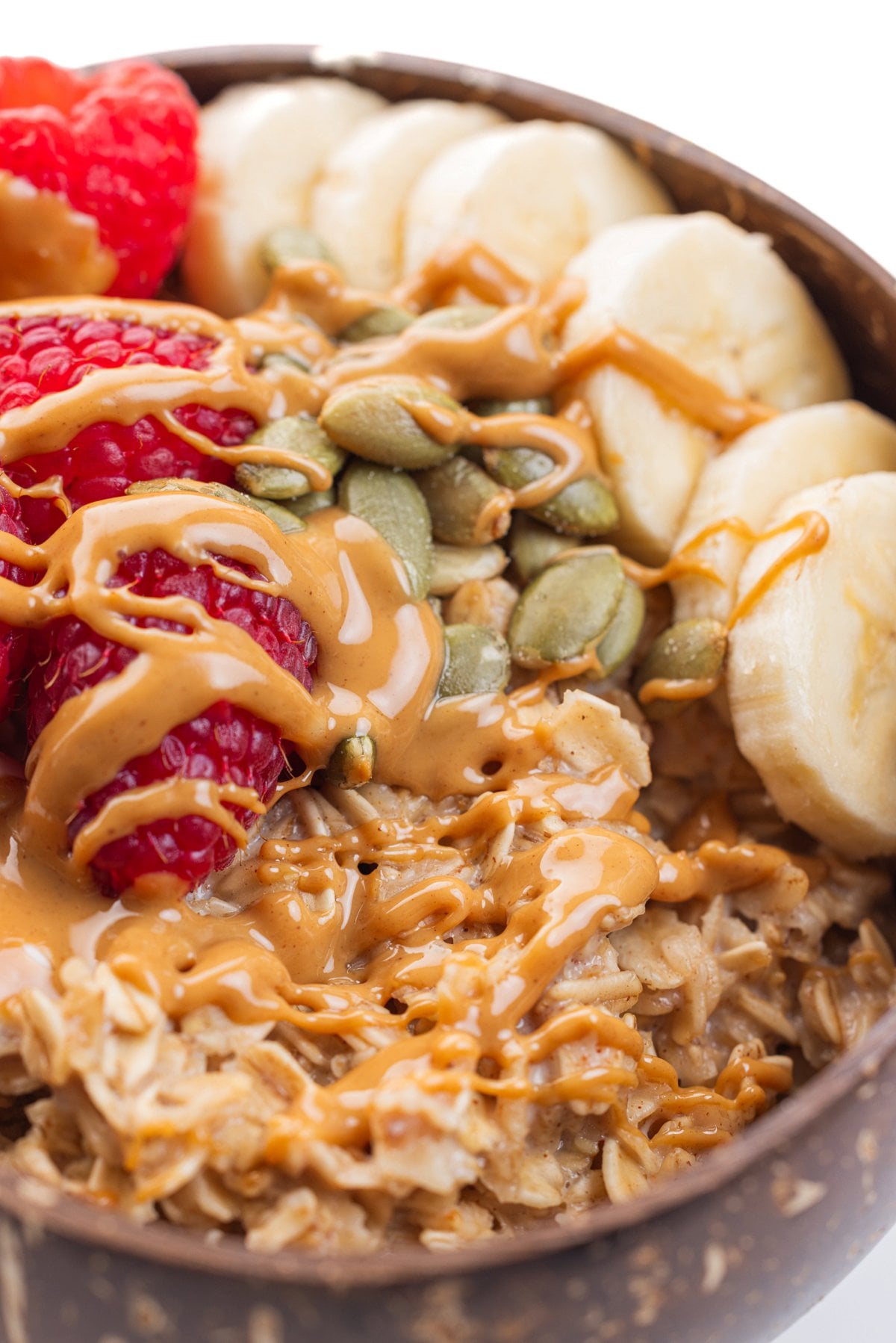 Close up shot of 90 second microwave oatmeal with pepitas, drizzled peanut butter, and fruit.