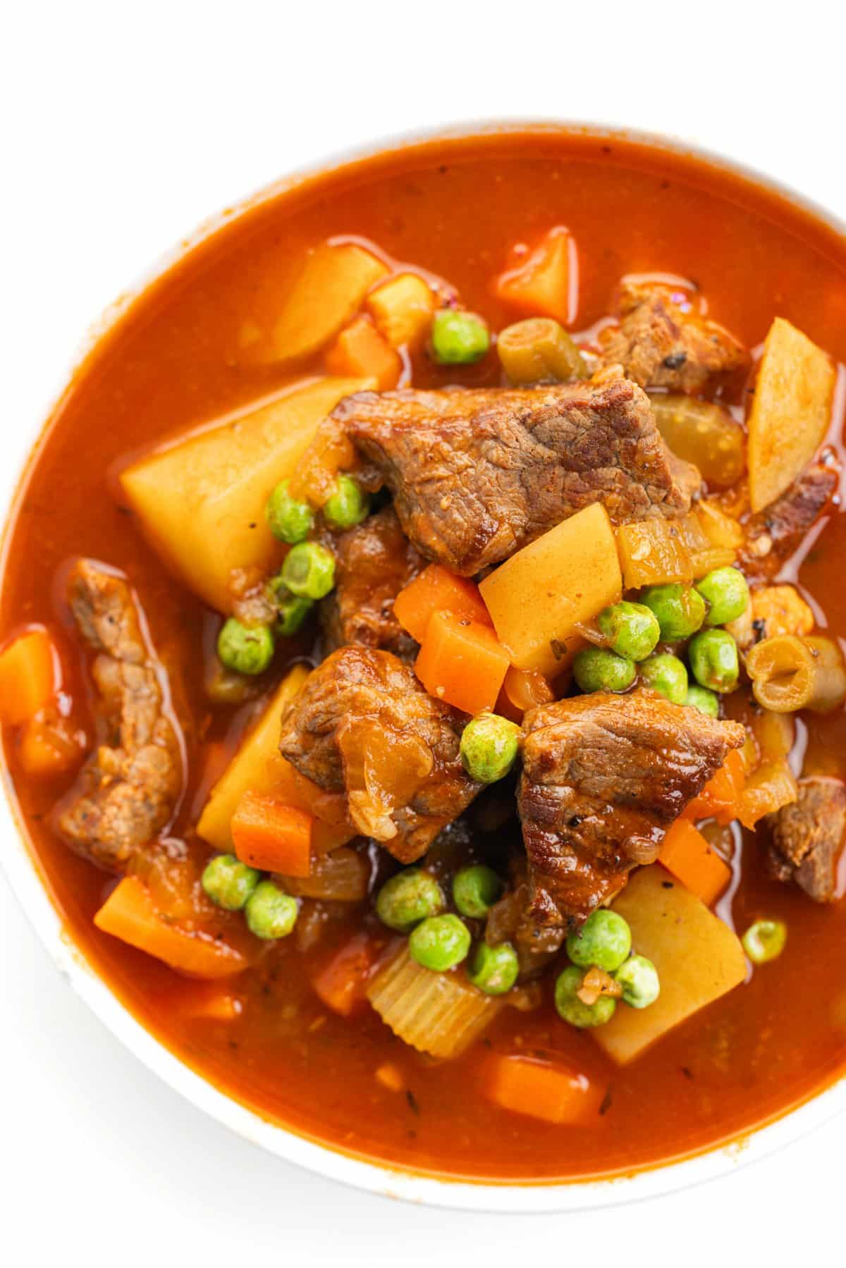 Top down view of vegetable beef soup in a white bowl.