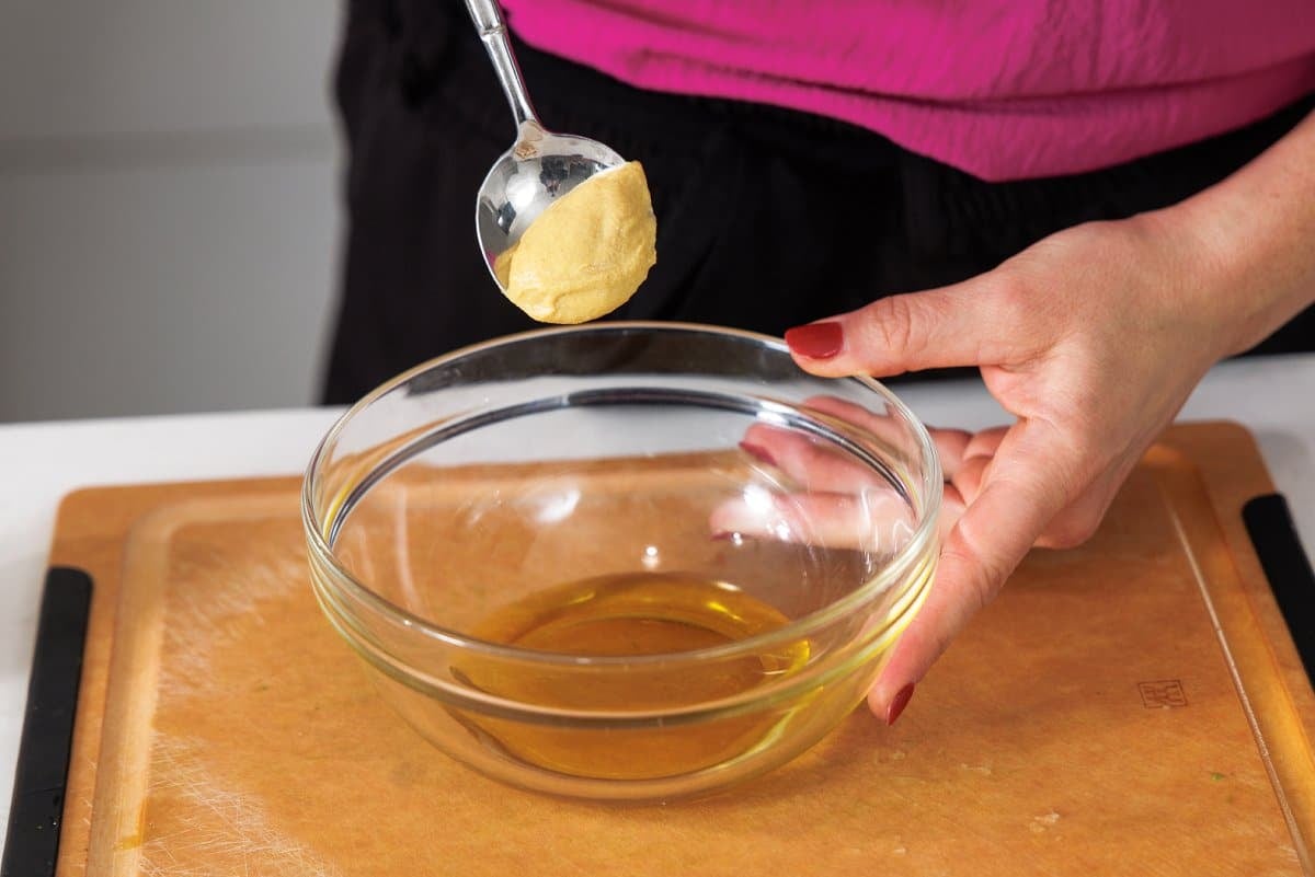 Adding a spoonful of dijon mustard to bowl with olive oil.