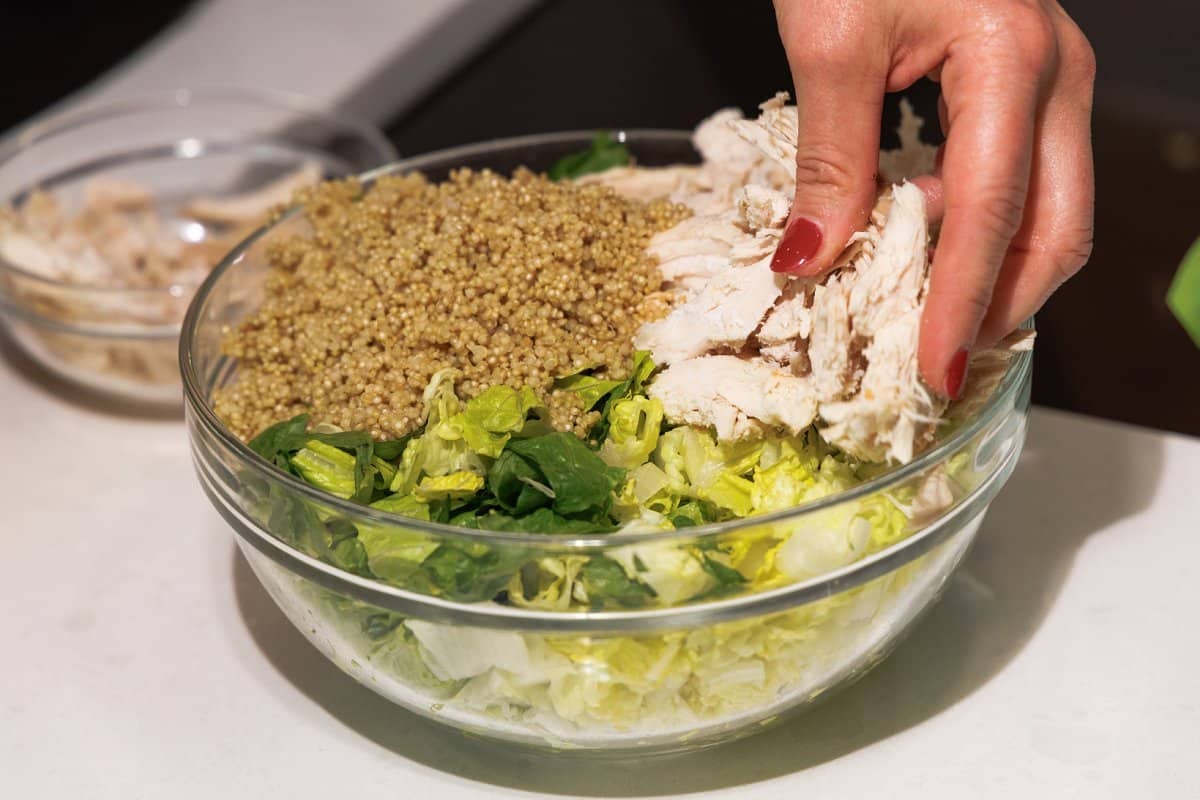 Placing shredded chicken in large bowl on top of lettuce.