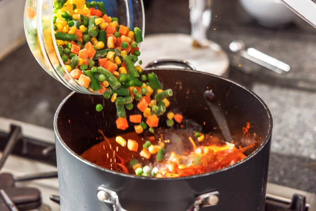 Adding frozen veggie mix to soup.