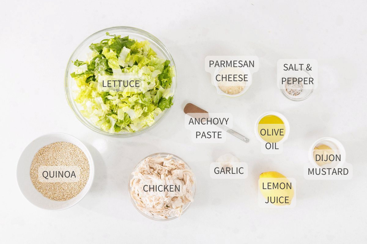 Labeled ingredients for chicken caesar salad bowls with quinoa on a white counter.
