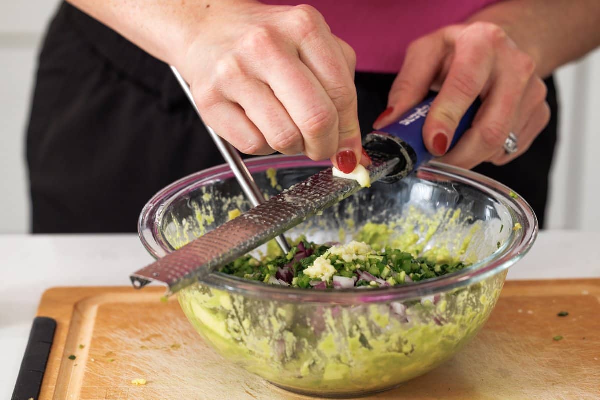 Using microplane to grate garlic into bowl.
