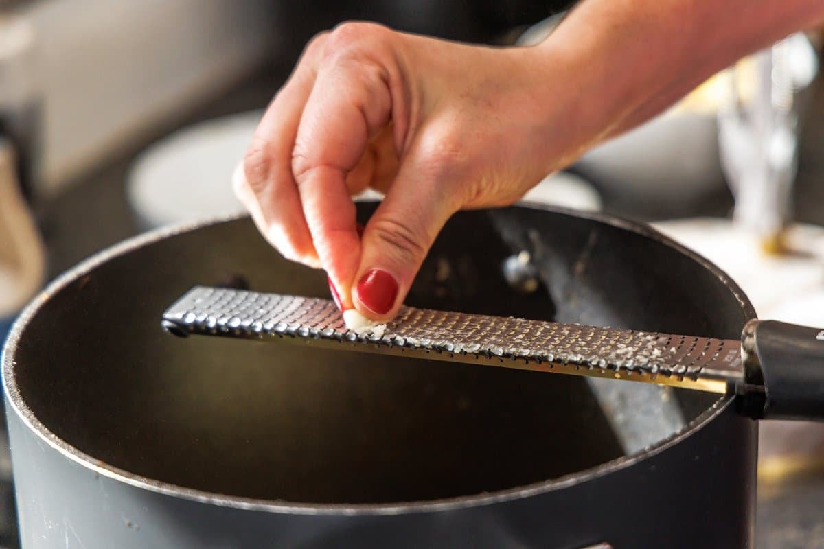 Grating garlic into soup pot with microplane.