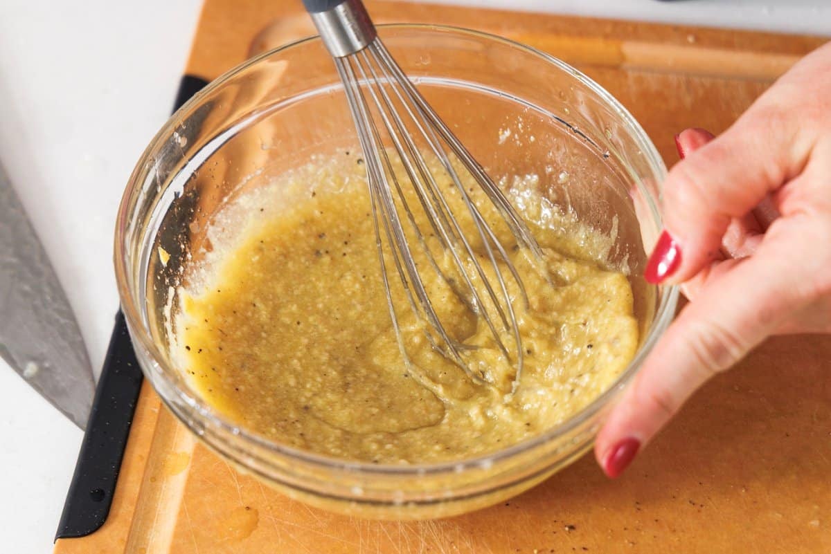Whisking together caesar dressing in glass bowl.