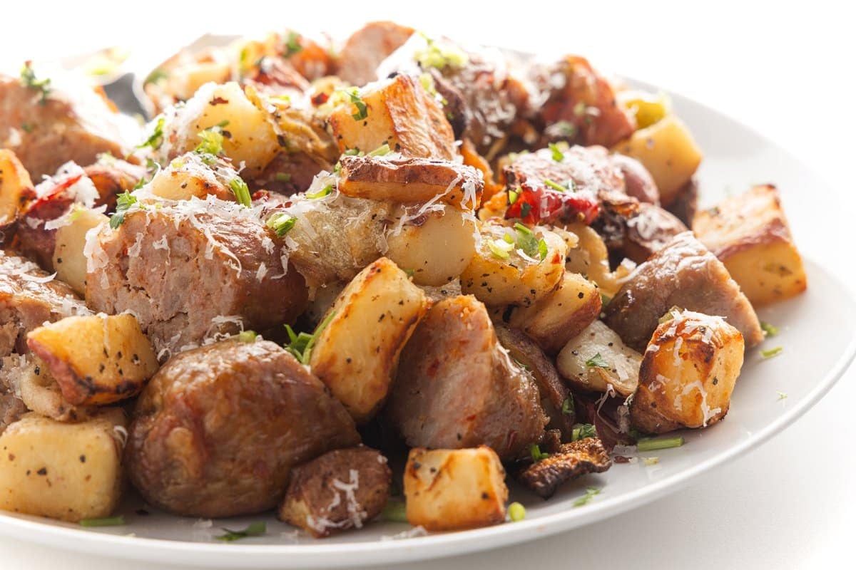 A plate of air fryer sausage, potatoes, and peppers garnished with parmesan cheese and fresh herbs.