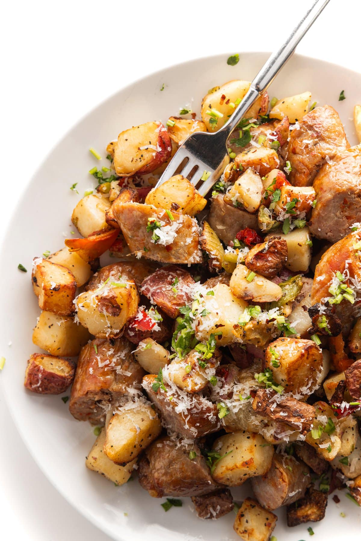 A plate full of air fryer sausage, potatoes, peppers, and onion with a fork.
