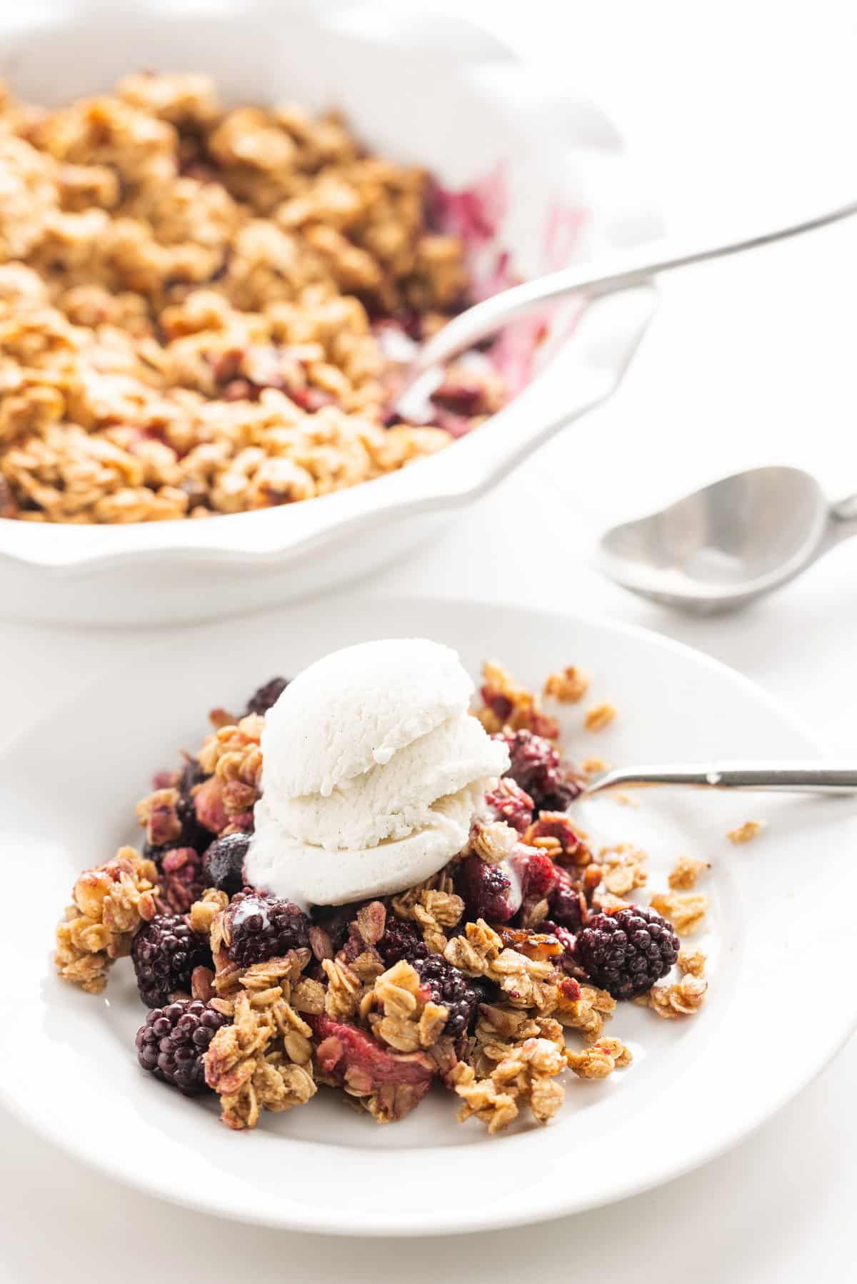 Pie dish of berry crisp and plate of berry crisp topped with vanilla ice cream.
