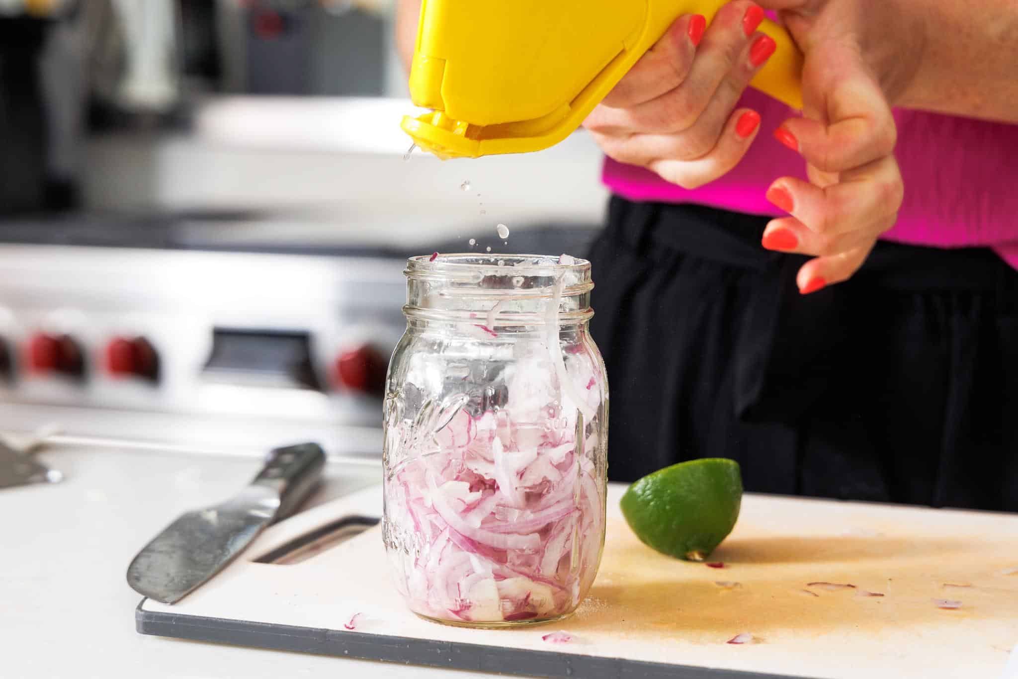 Squeezing lime juice over sliced red onion in a jar.