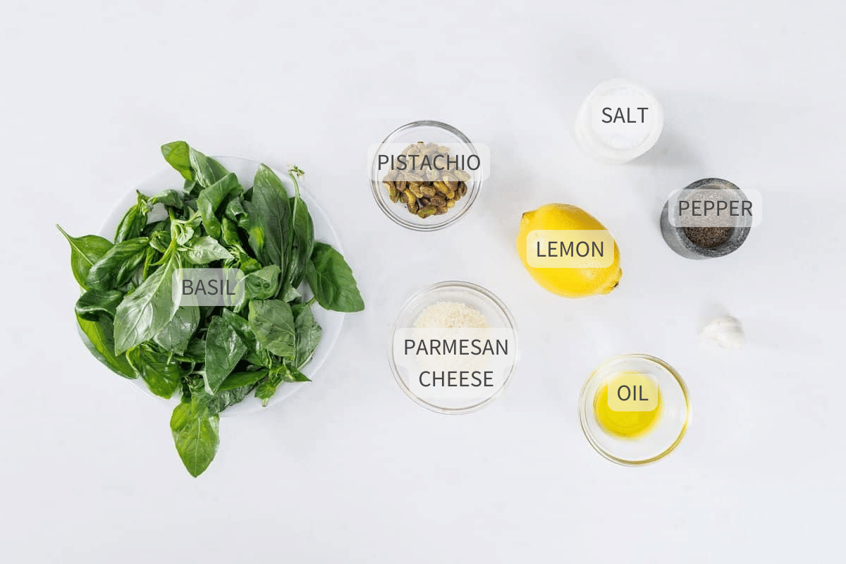 Labeled ingredients for basil pistachio pesto on a white counter.