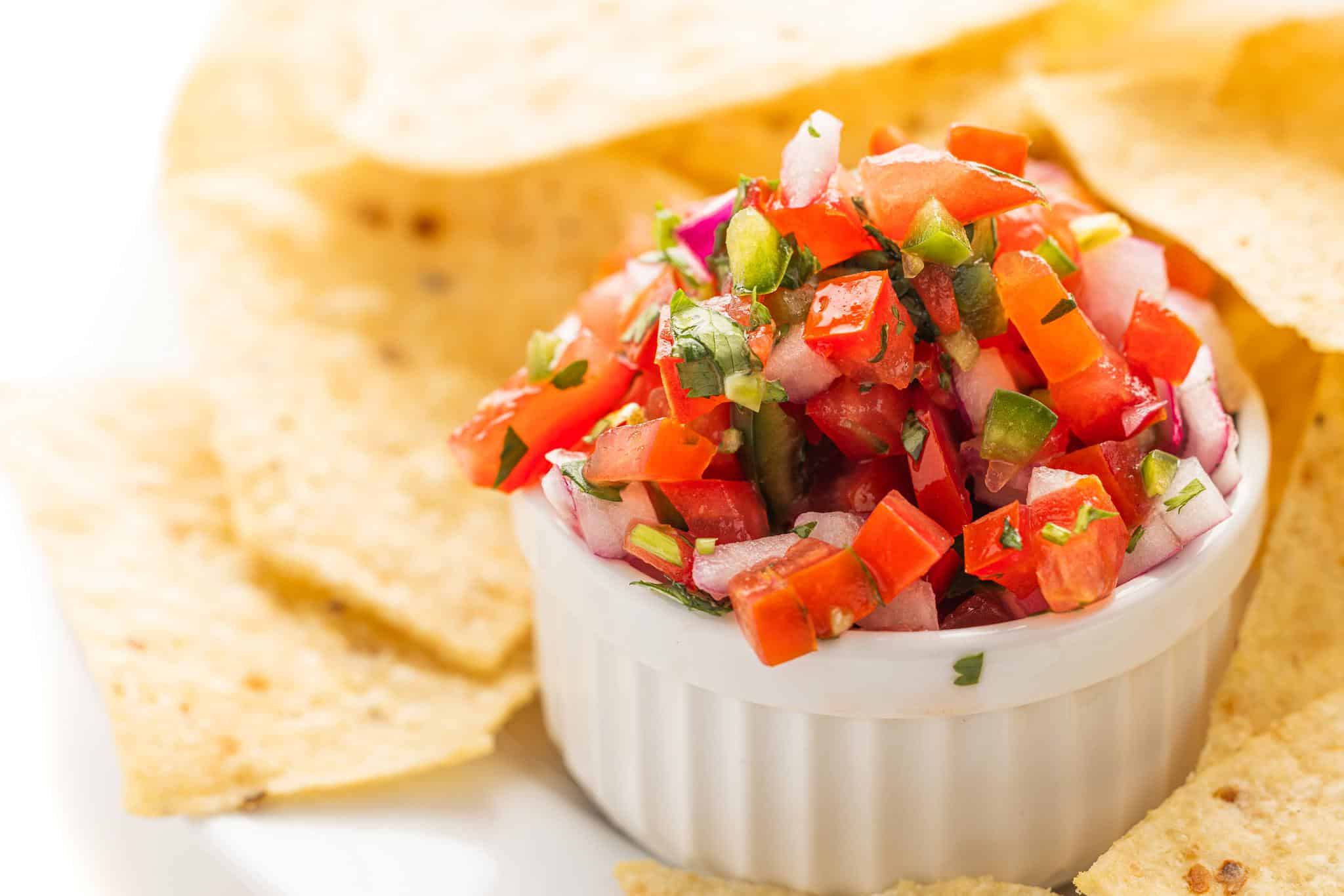 Ramekin of fresh pico de gallo on a plate with tortilla chips.