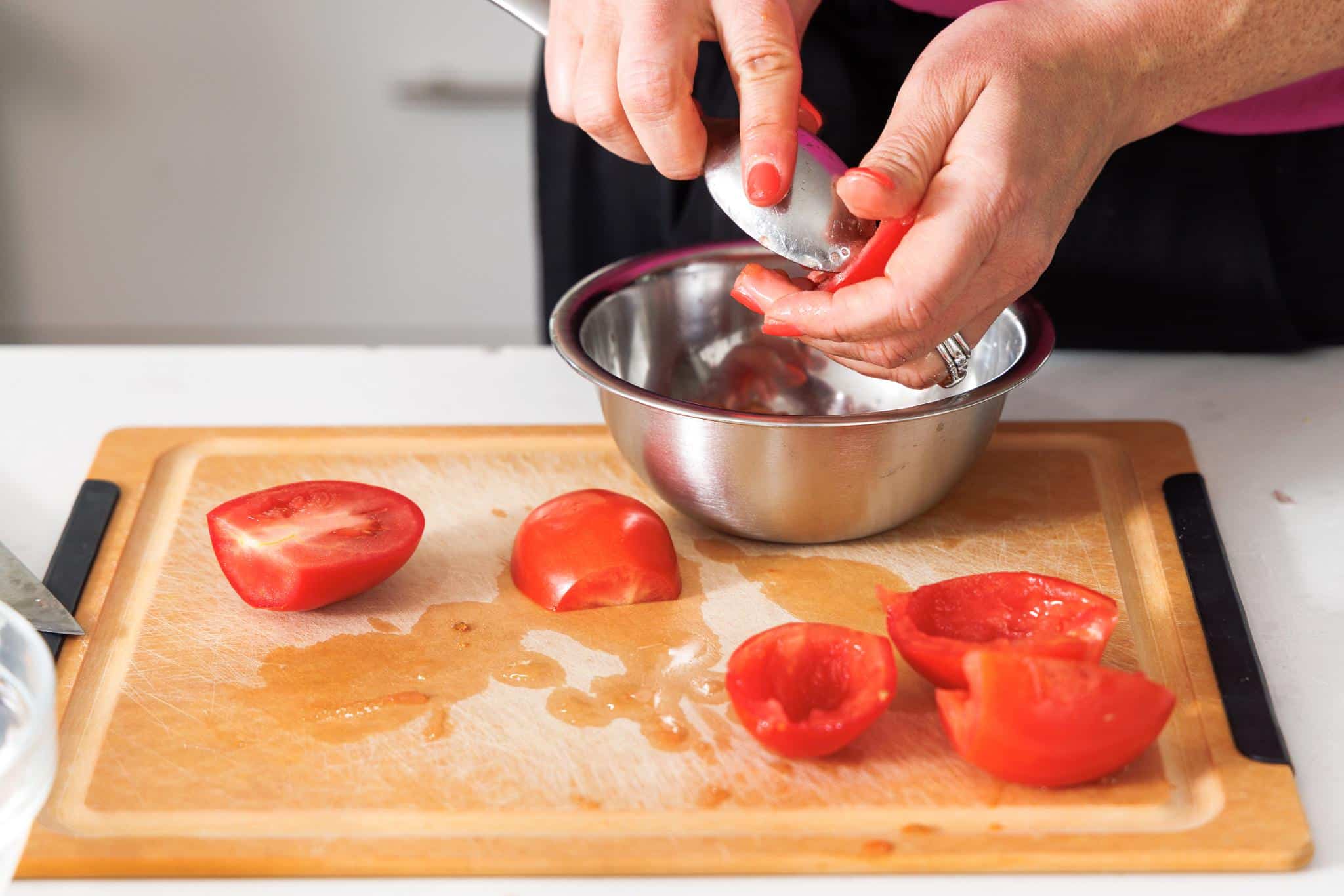 Cleaning out center of Roma tomatoes with a spoon.