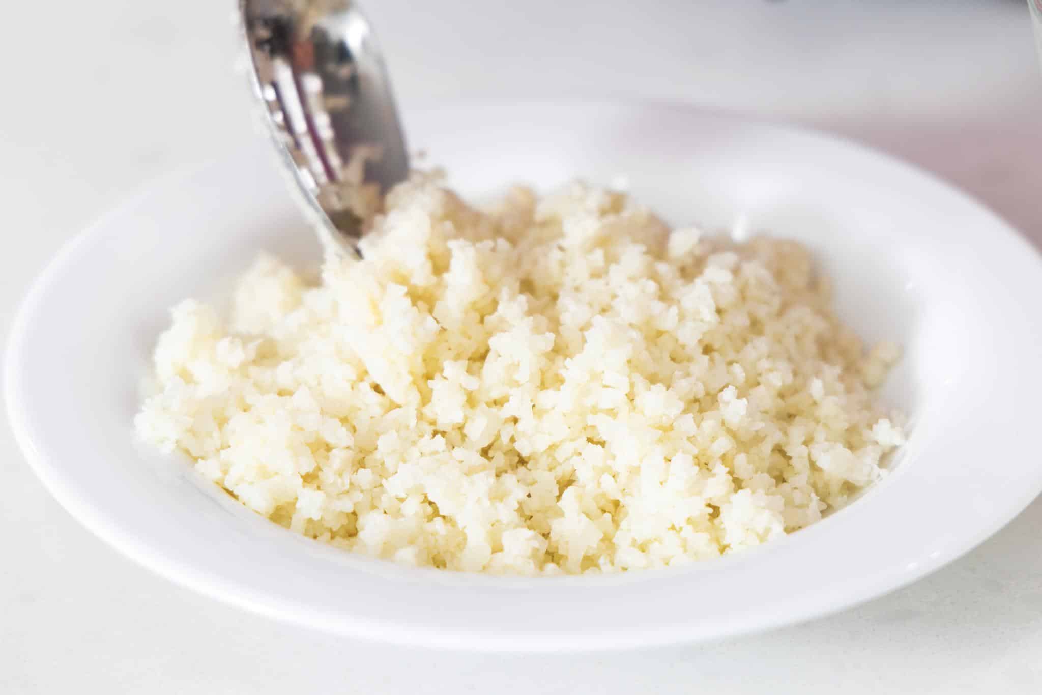 Putting cooked cauliflower rice in a shallow bowl.