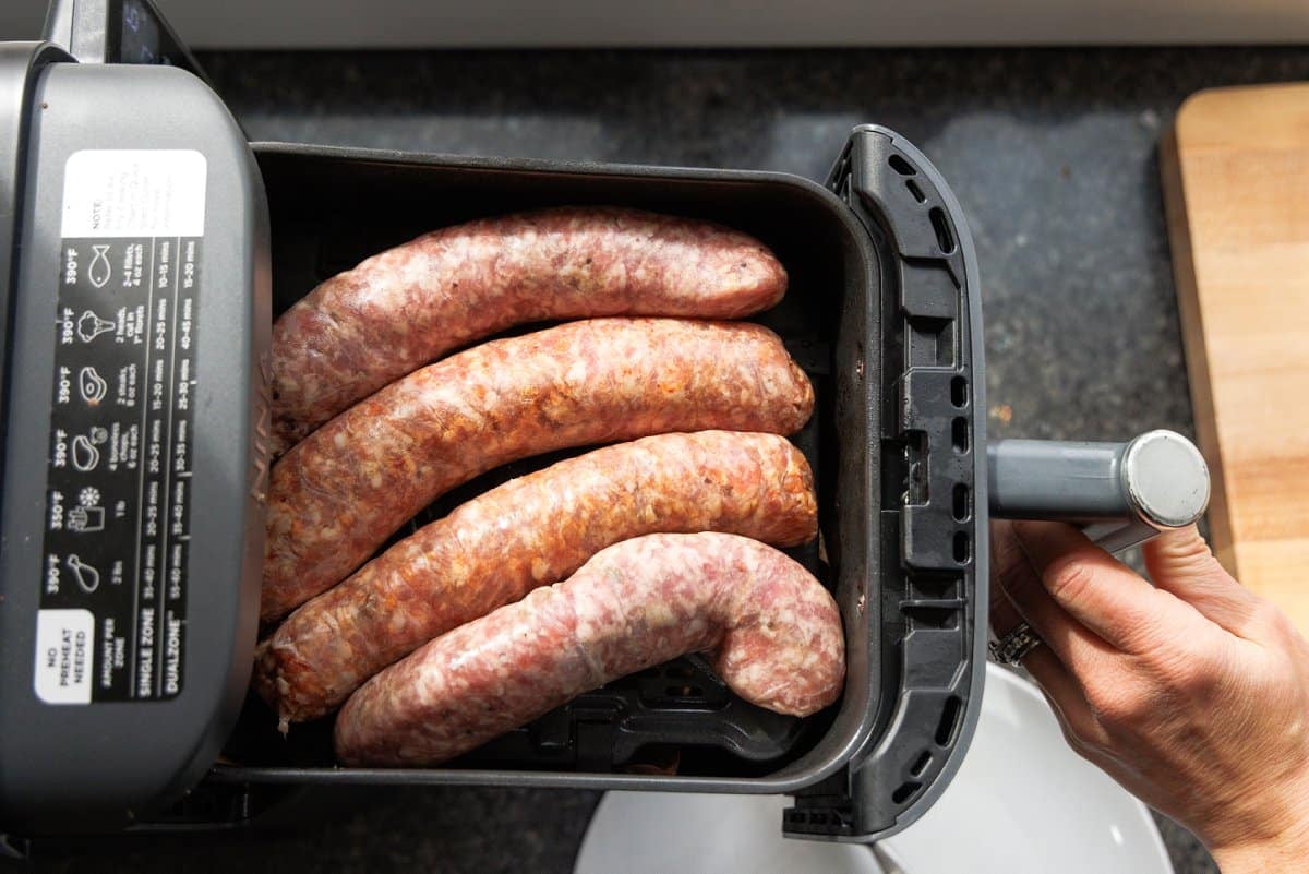 Four uncooked sausage links in an air fryer basket.