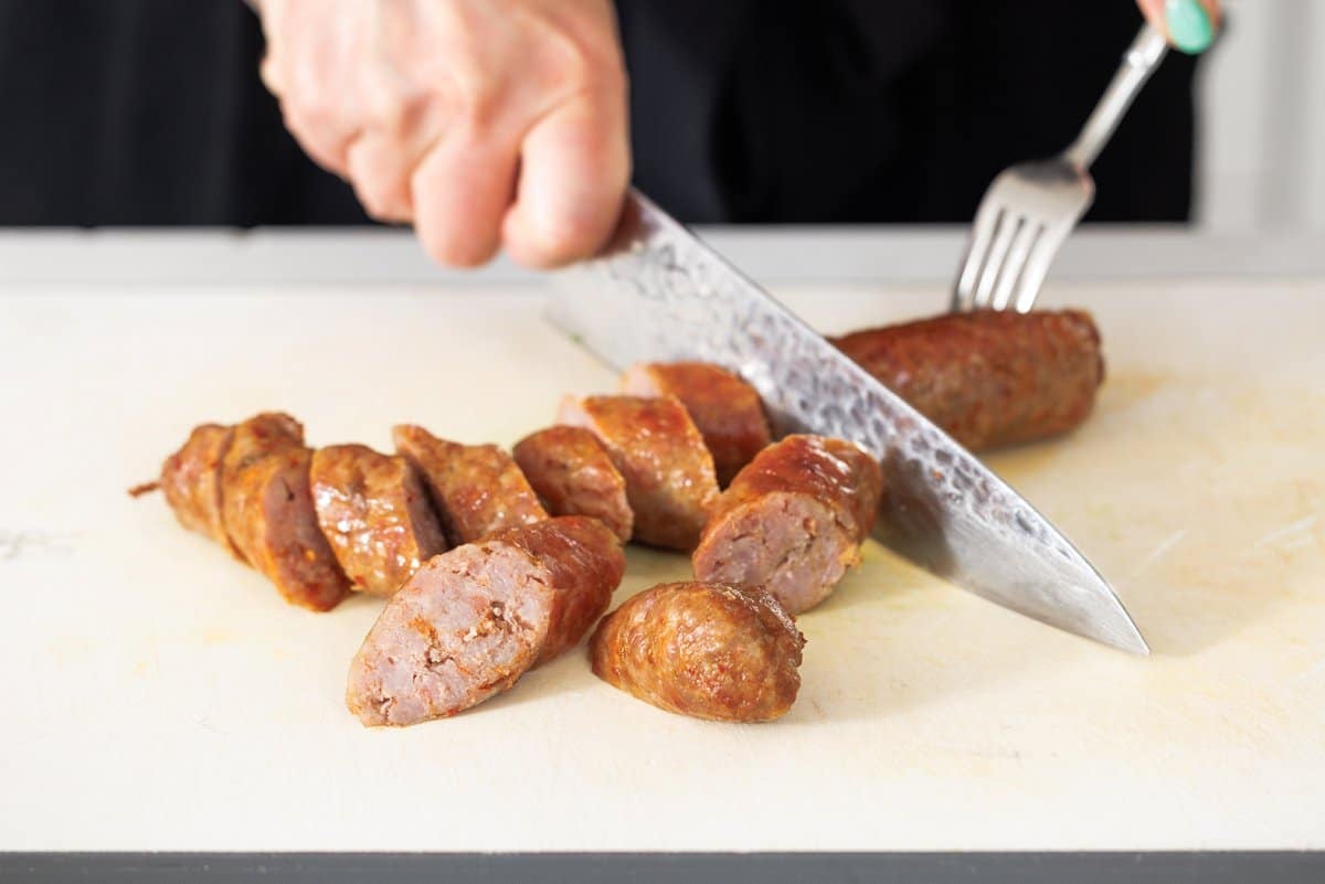 Cutting cooked sausage links on a cutting board.