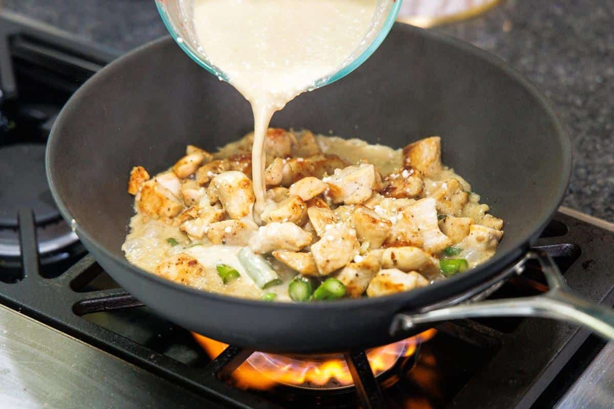 Pouring curry sauce over chicken and asparagus in woke.